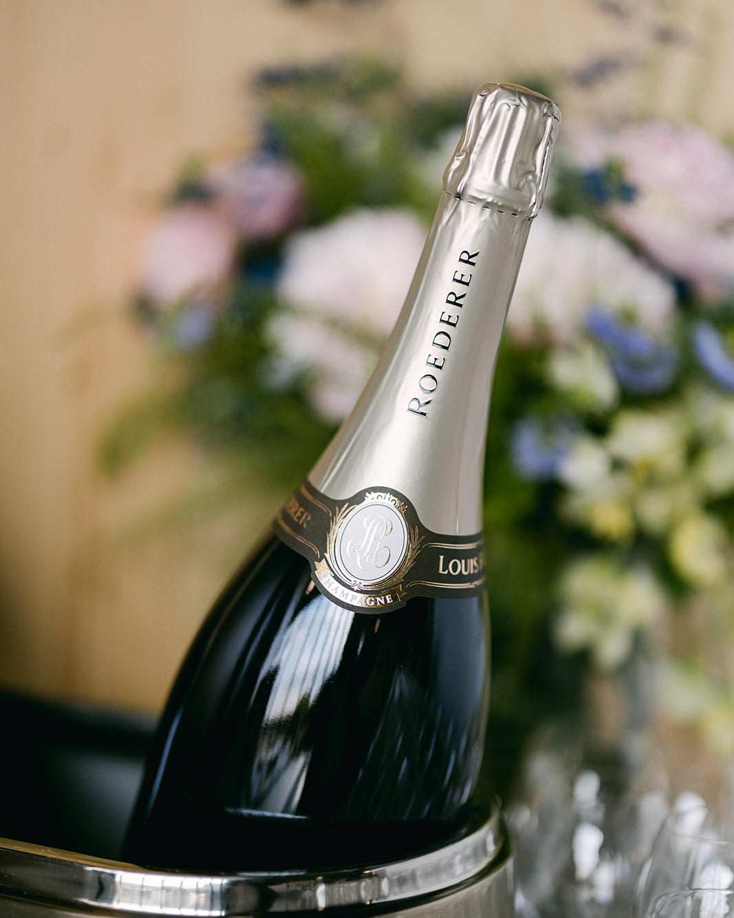 Bottle of Roederer champagne in an ice bucket with flowers in the background