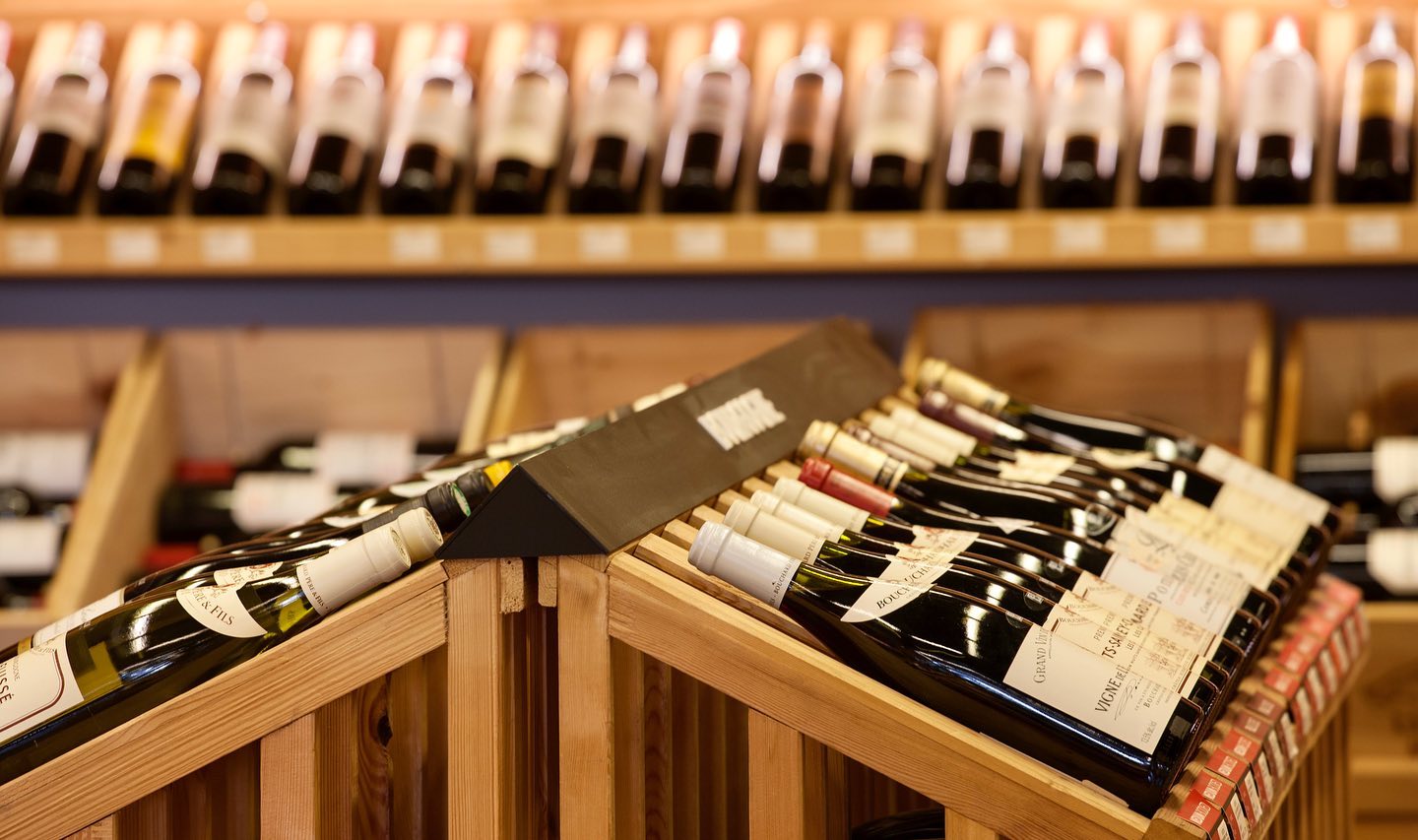 Wine bottles displayed on a wooden rack with a blurred background of more wine bottles.