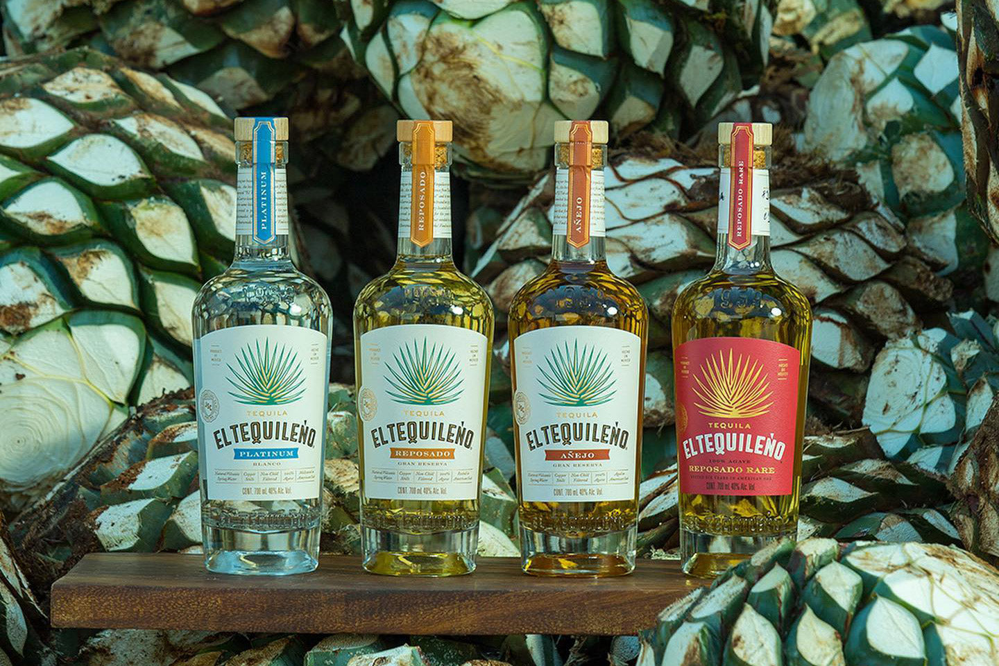 Four bottles of El Tequileno tequila on a wooden shelf with agave plants in the background.